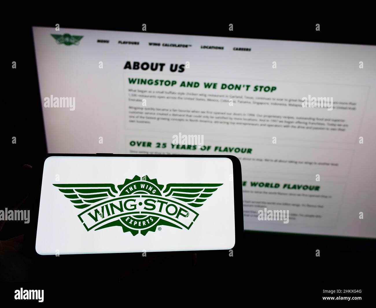 Person mit Mobiltelefon und Logo des US-Gastronomieunternehmens Wingstop Restaurants Inc. Auf dem Bildschirm vor der Webseite. Konzentrieren Sie sich auf die Telefonanzeige. Stockfoto