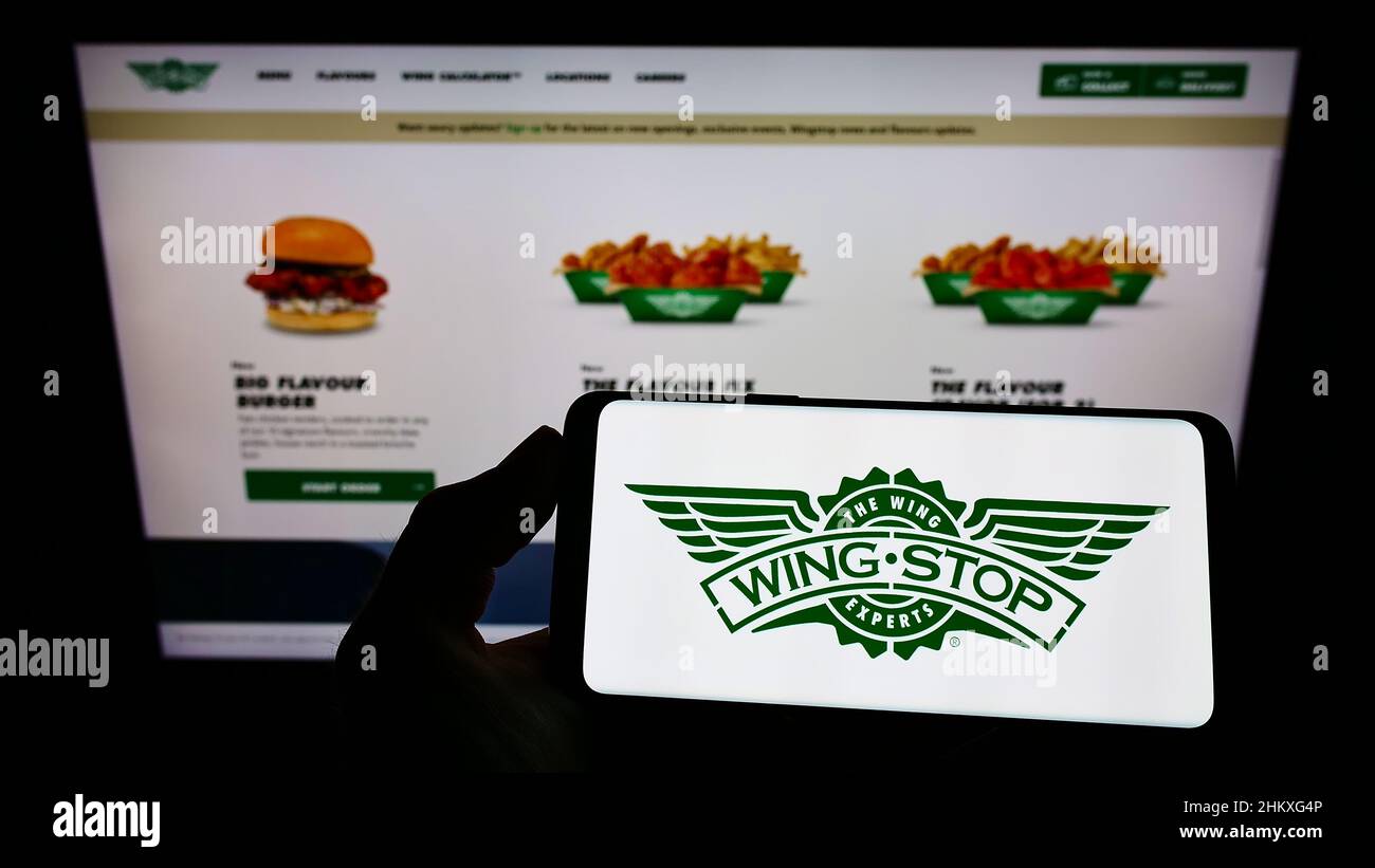 Person, die Mobiltelefon mit dem Logo des amerikanischen Gastronomieunternehmens Wingstop Restaurants Inc. Auf dem Bildschirm vor der Website hält. Konzentrieren Sie sich auf die Telefonanzeige. Stockfoto