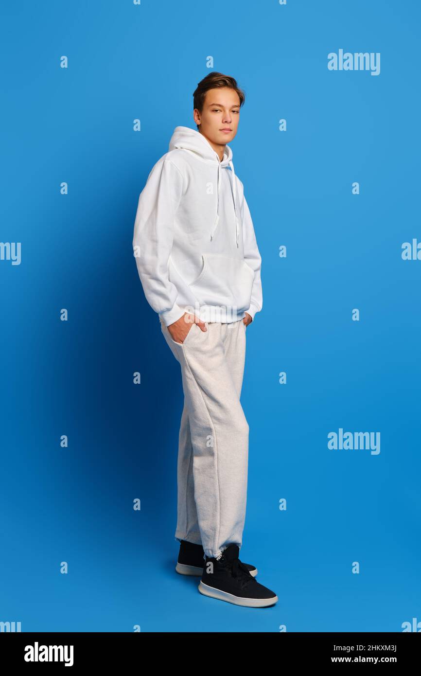 Junger Mann mit weißem Sweatshirt und Sweatshirts auf blauem Studiohintergrund mit Händen in den Taschen Stockfoto