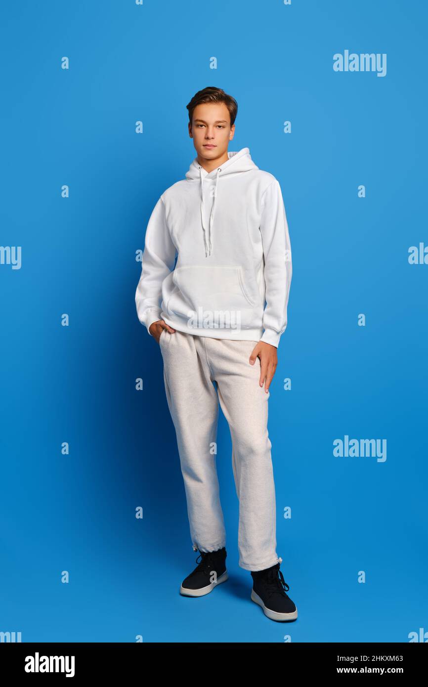 Attraktiver, stilvoller Mann mit weißem Sweatshirt und Sweatshirts, der auf blauem Studiohintergrund steht Stockfoto