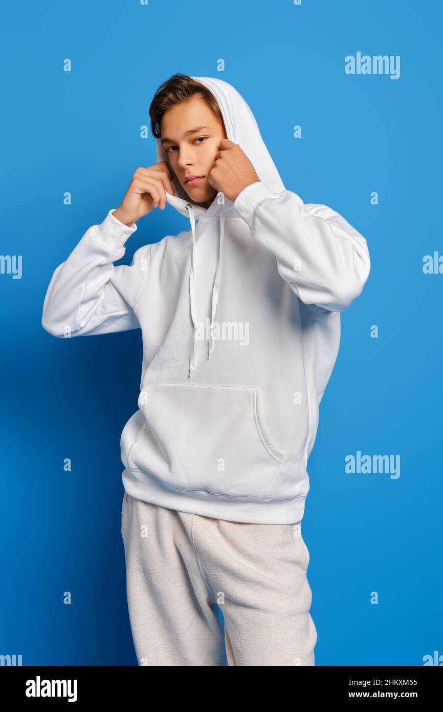 Nachdenklicher junger Mann in weißer Schweißaufnahme zieht sich auf den blauen Studiohintergrund Stockfoto
