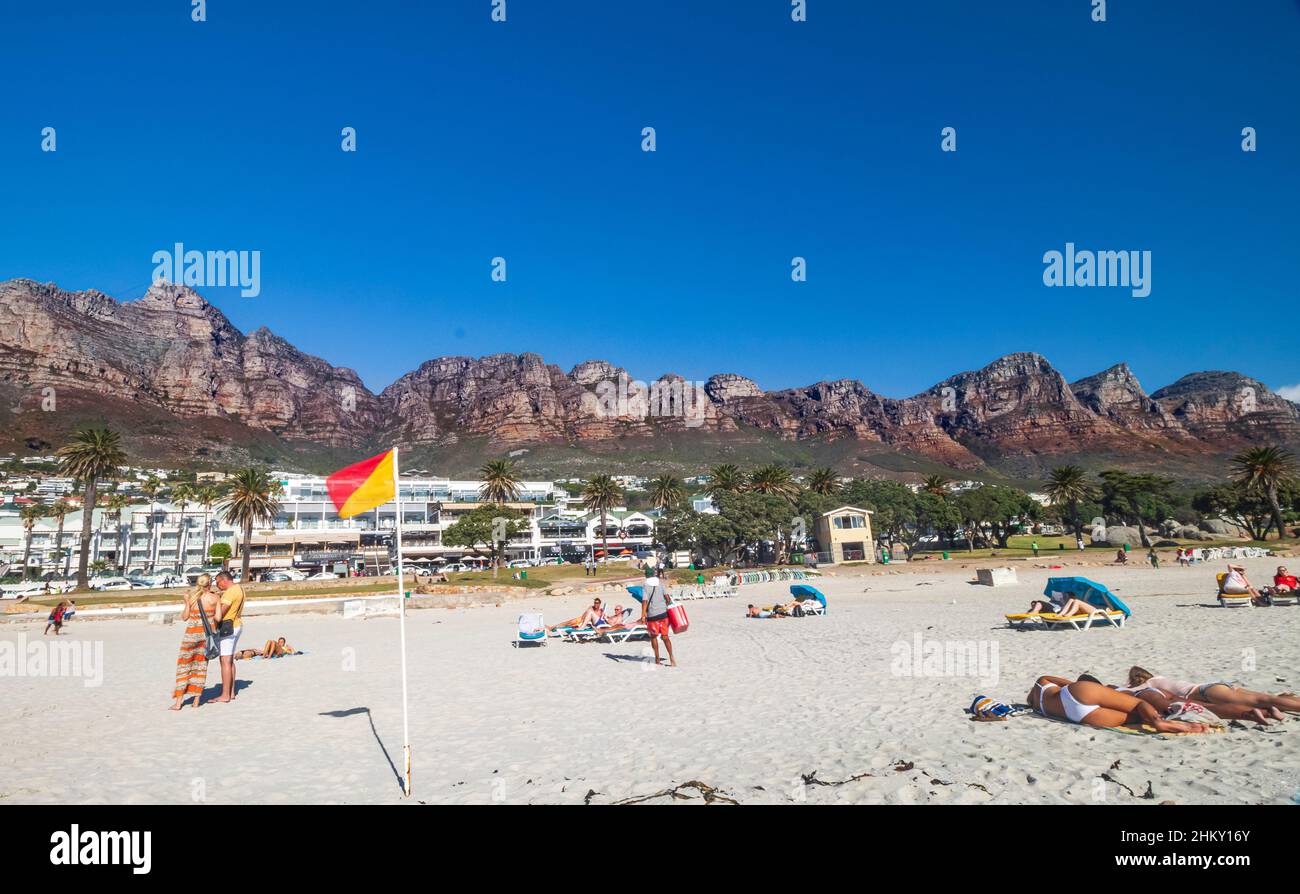 Camps Bay Beach mit Sonnenanbetern und Twelve Apostles Mountain Ranges am Tafelberg im Hintergrund, am Rande von Kapstadt, Südafrika. Stockfoto