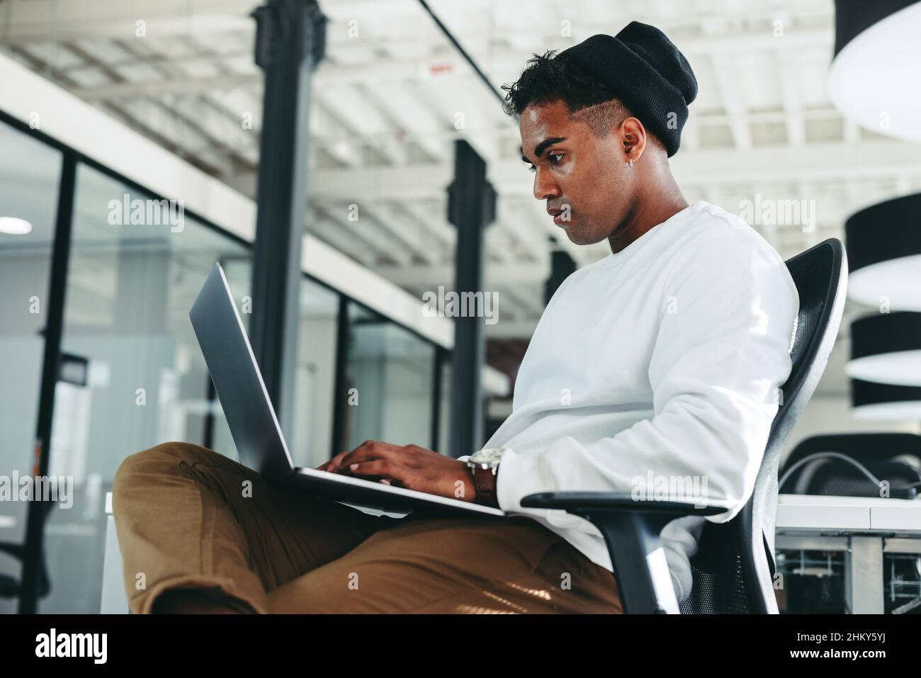 Junger Programmierer, der in einem modernen Büro an einem neuen Code arbeitet. Fokussierter junger Geschäftsmann mit einem Laptop an einem modernen Arbeitsplatz. Kreative Geschäftsmusik Stockfoto