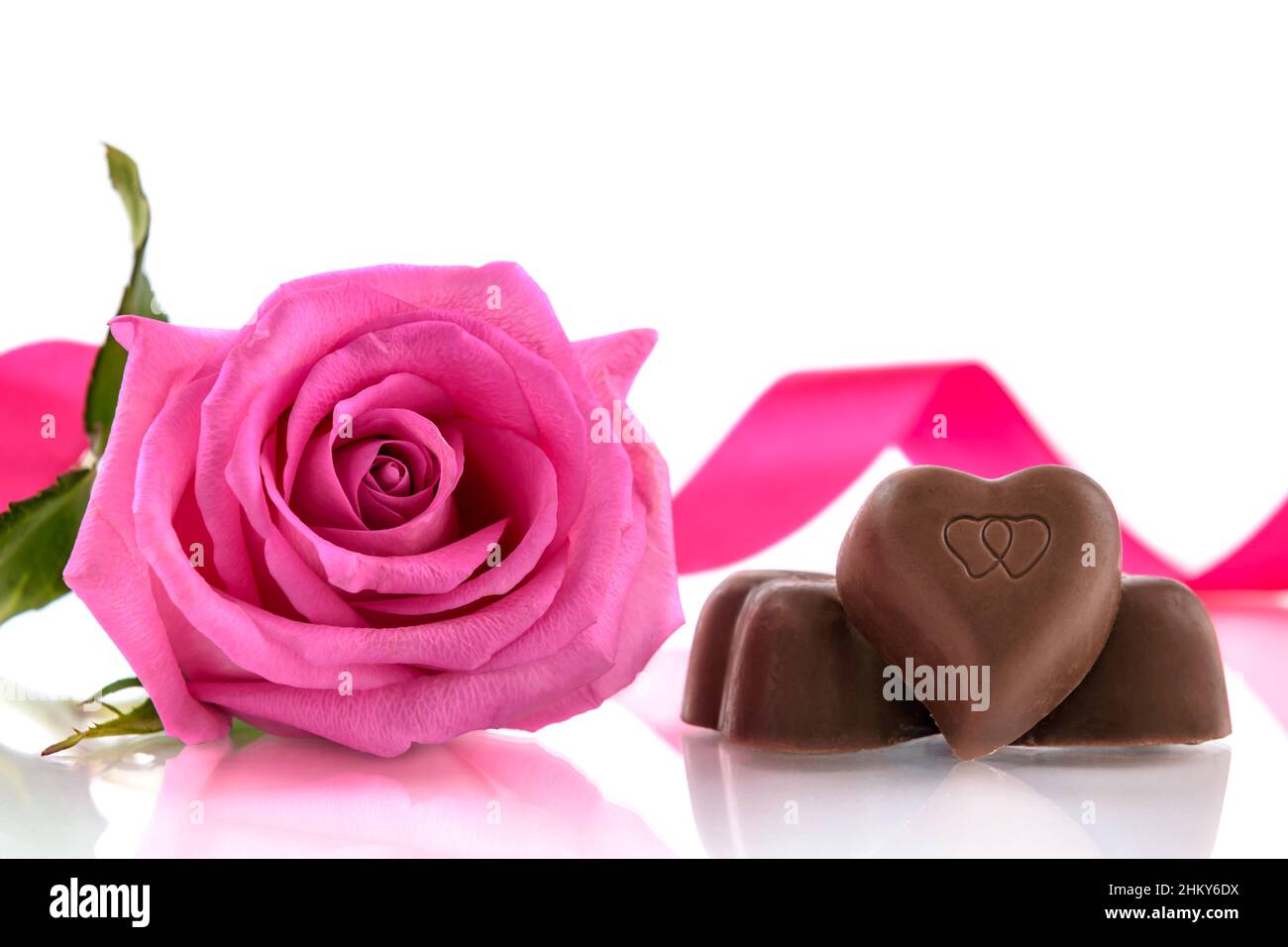Drei herzförmige Pralinen und rosa Rose auf weißem Hintergrund. Valentinstagskonzept, selektiver Fokus. Stockfoto
