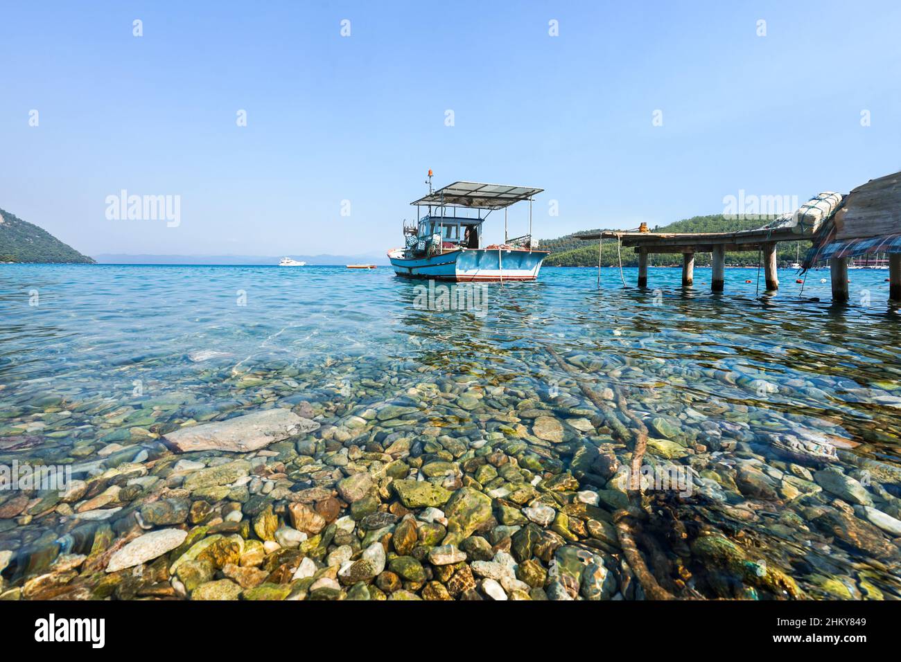 Ein blaues kleines Fischerboot im Meer, das im Hafen mit einem Seil gebunden ist. Klare Sicht auf den Strand von Akbuk Cove (Bucht) in der Provinz Mugla im Südwesten der Türkei. Stockfoto