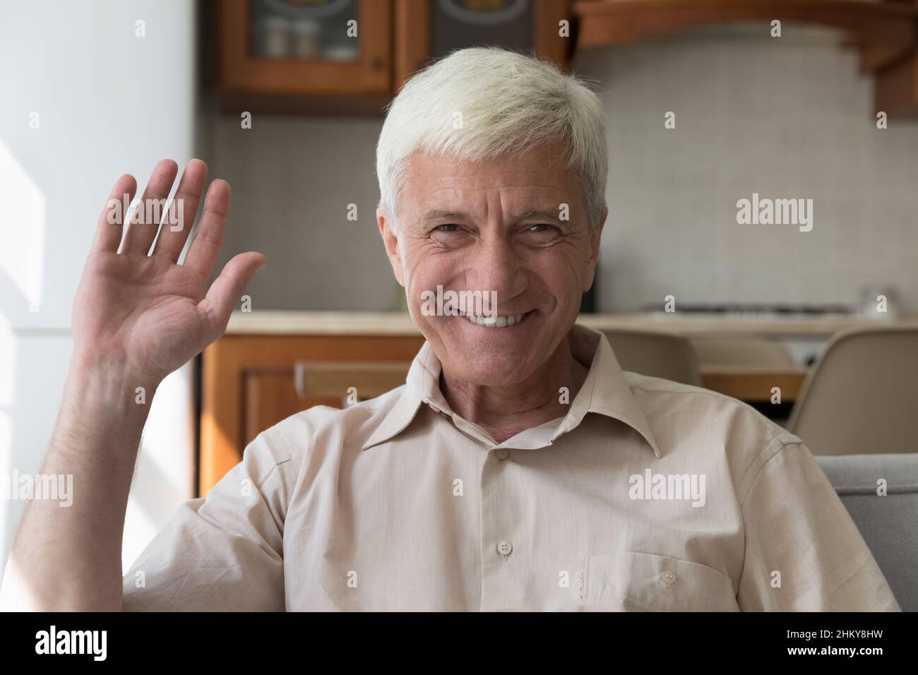 Glücklicher älterer 60s-Mann, der die Kamera anlächelt und mit der Hand hallo winkt Stockfoto