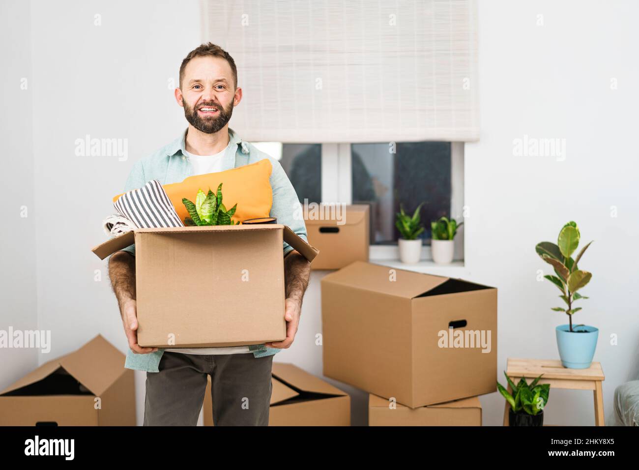 Reifer Mann, der eine Umzugskiste mit Kissen trägt und in eine neue Wohnung zieht Stockfoto