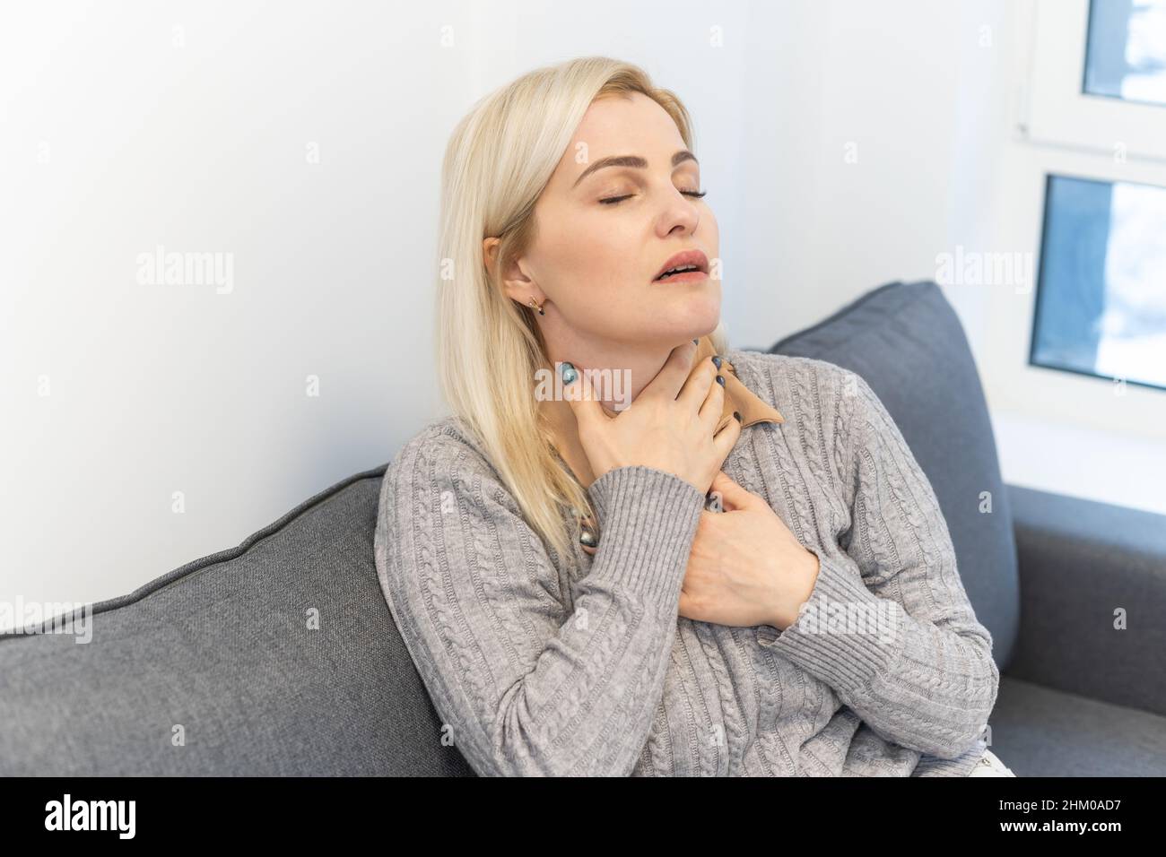 Attraktive Frau sitzt auf dem Bett mit Halsschmerzen Stockfoto