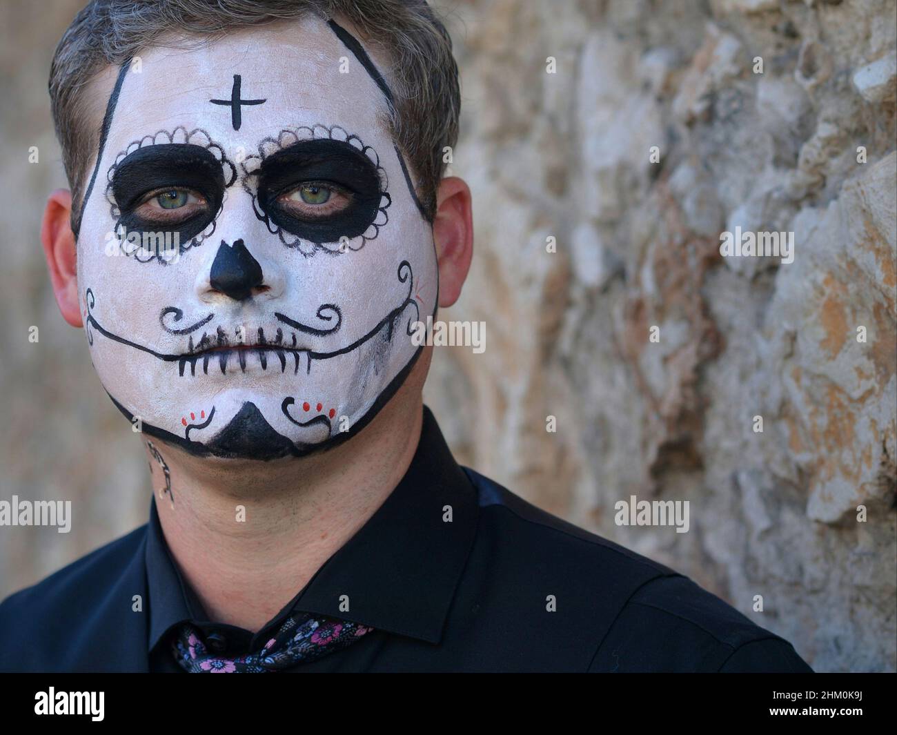 Der junge kaukasische Mann mit gruseliger traditioneller weißer Gesichtsmalerei am Tag der Toten (Día de los Muertos) sieht den Betrachter ernsthaft an. Stockfoto