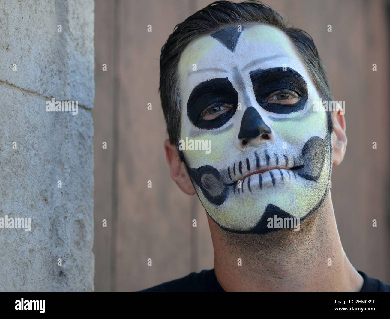 Der junge kaukasische Mann mit gruseliger traditioneller weißer Gesichtsmalerei am Tag der Toten (Día de los Muertos) blickt auf den Betrachter herab. Stockfoto
