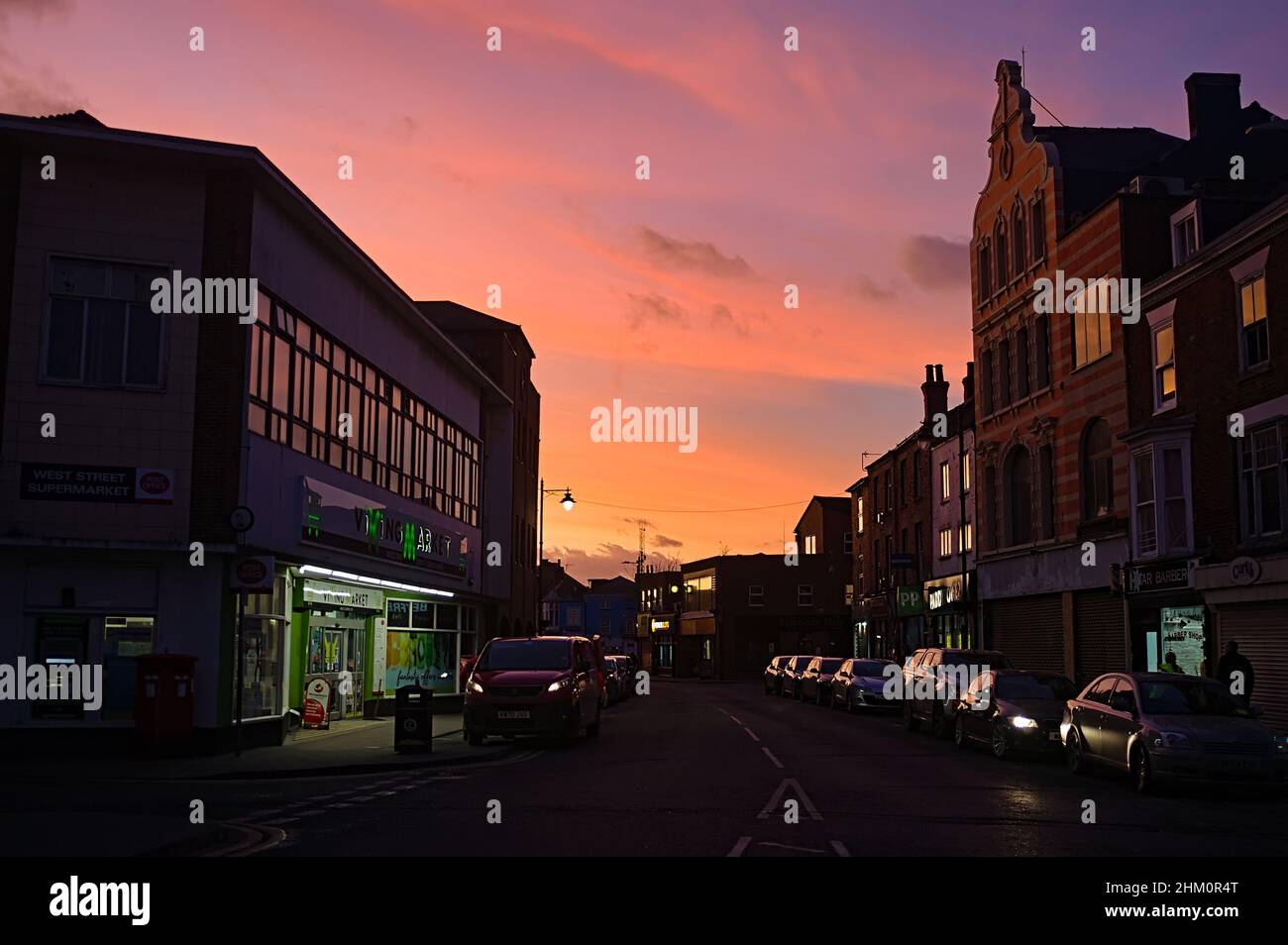 Blick auf die West Street mit geparkten Autos und europäischen Geschäften bei Sonnenuntergang. Stockfoto
