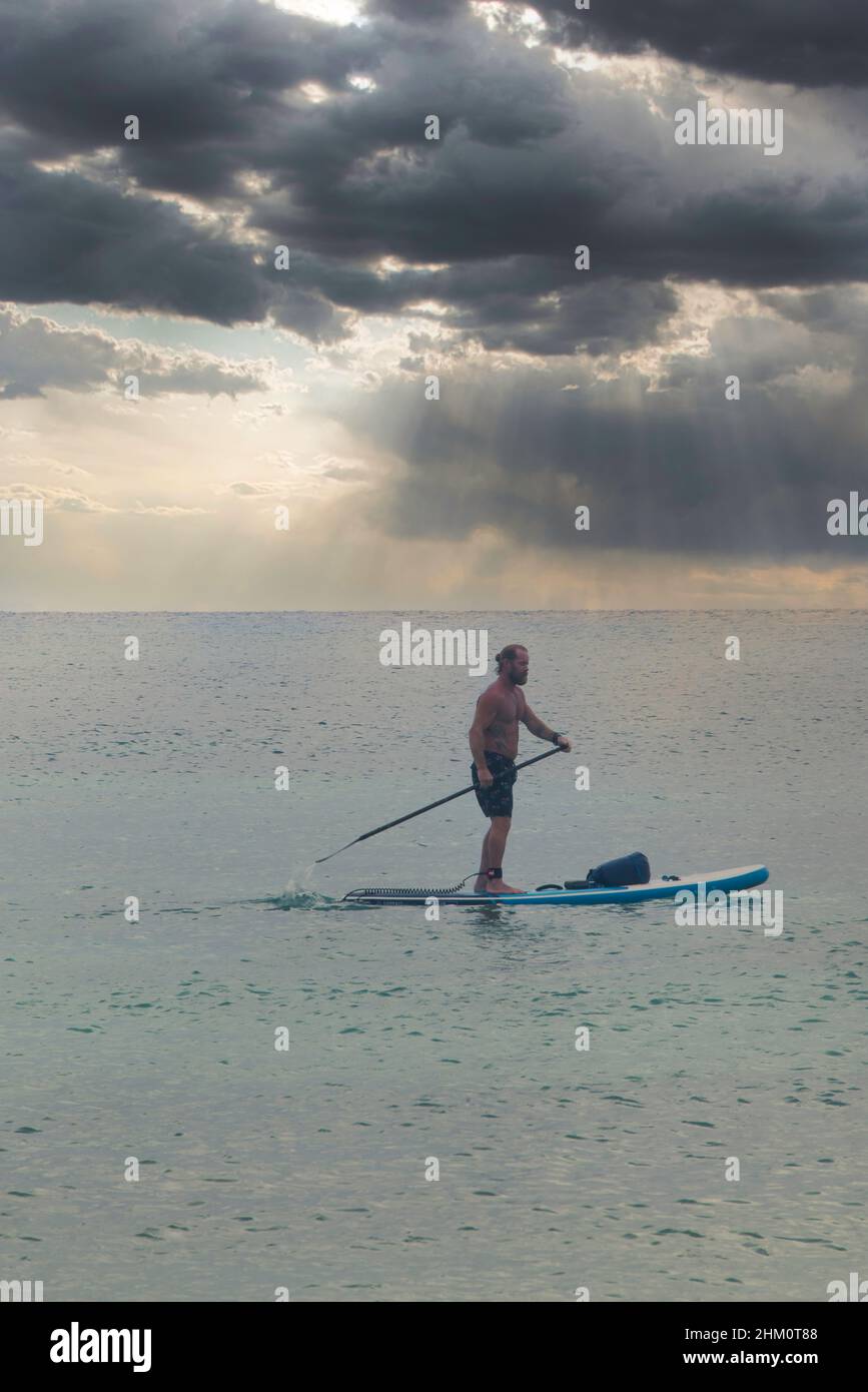 Ein Sportler navigiert auf einem Paddelbrett in der Karibik vor einem dramatischen Himmel in Mexiko Stockfoto