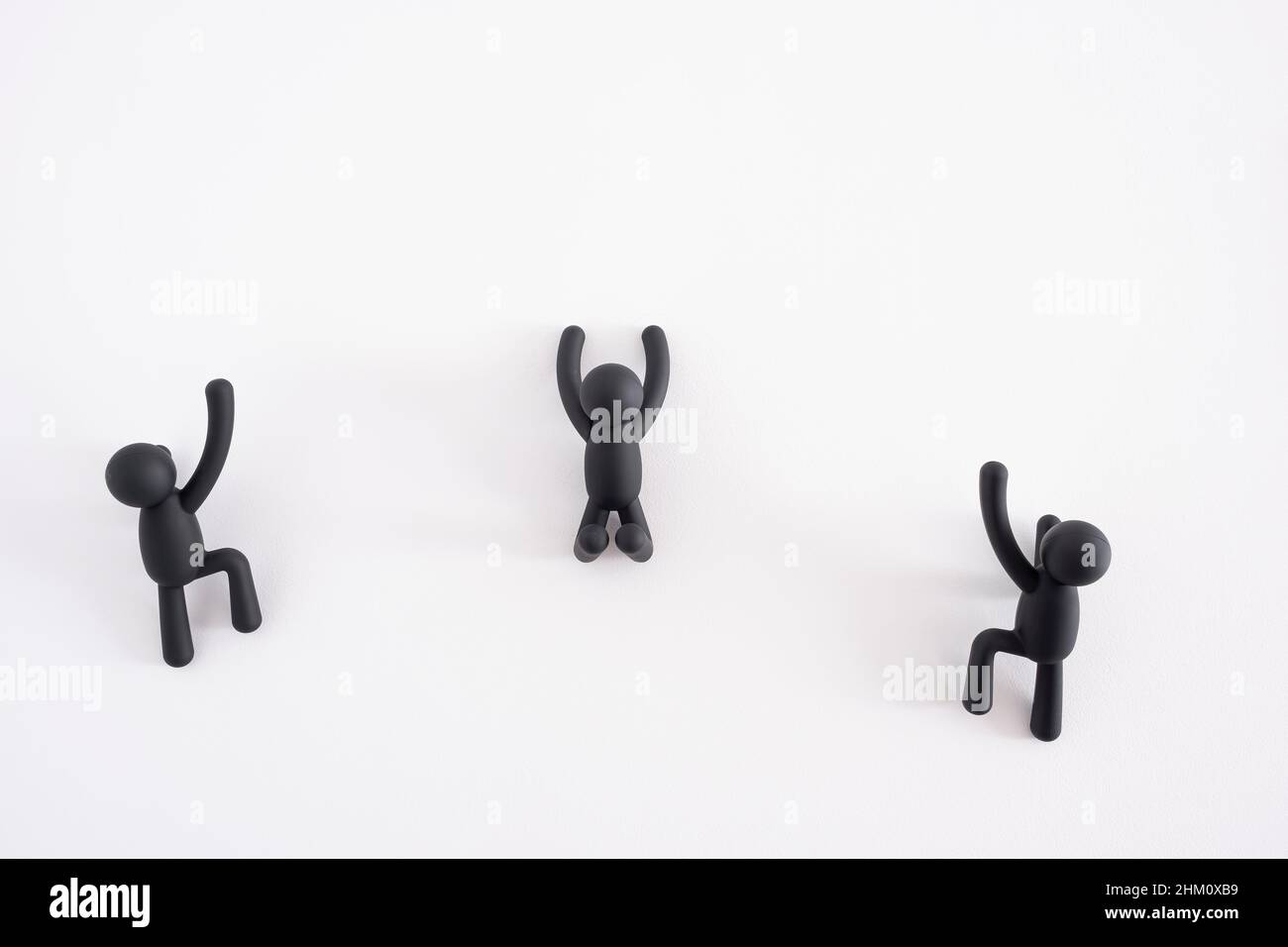 Drei schwarze 3D Marionetten, die über einen weißen Hintergrund klettern, 3D Menschen, menschlicher Charakter, Person, die an einer weißen Wand hängt, Konzept der Selbstverbesserung Stockfoto