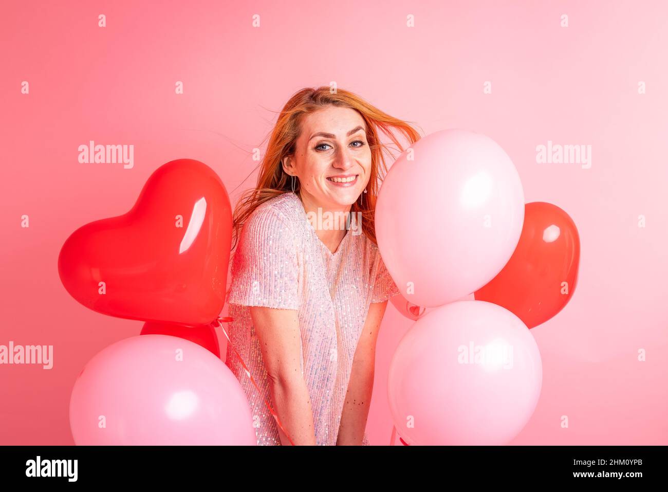 Schöne rothaarige Mädchen mit rotem Herz Ballon posiert. Alles Liebe zum Valentinstag Konzept. Studio Foto von schönen Ingwer Mädchen tanzen auf rosa Hintergrund. Stockfoto