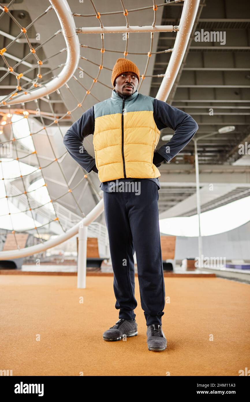 Junger ernsthafter afroamerikanischer Athlet, der auf einem Sportplatz mit Einrichtungen gegen ein Seilnetz zum Hochziehen und Krähen steht Stockfoto