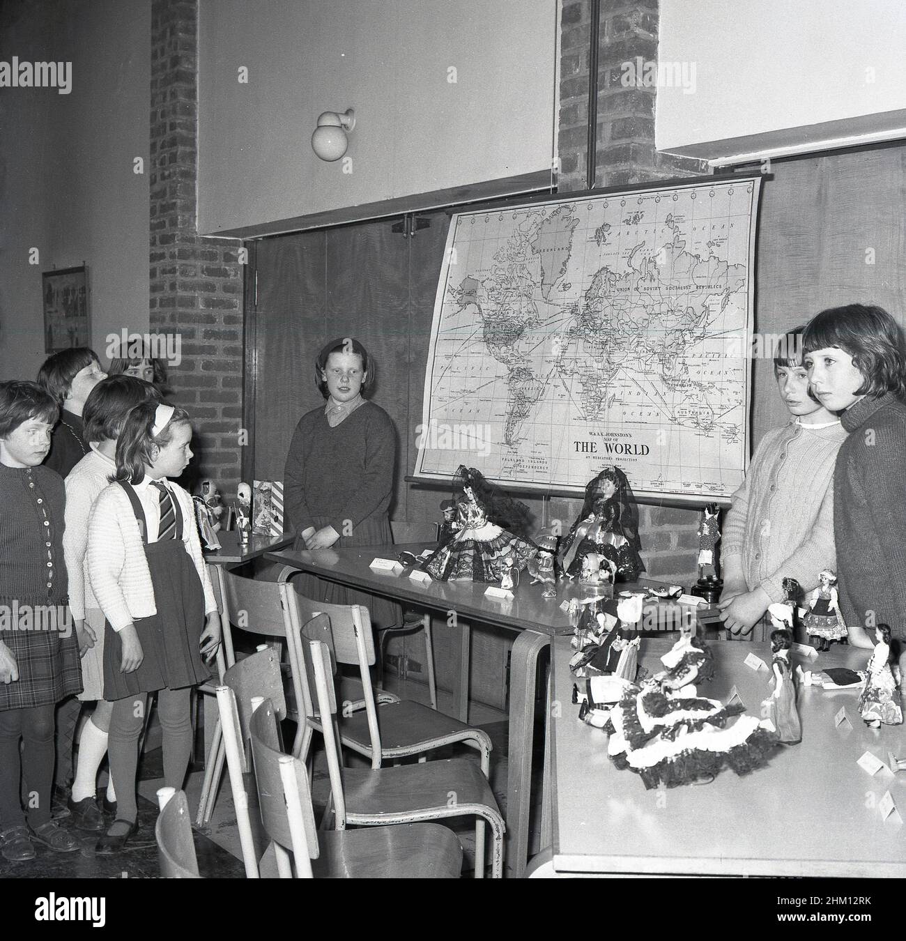 1960s, historisch, Grundschule, Puppen aus verschiedenen Ländern auf Tischen, mit Weltkarte an der Wand, Schottland, Großbritannien. Puppen sind in der Regel ein gekleidetes Modell eines menschlichen Charakters und wurden oft als Spielzeug oder Spielzeug verwendet, insbesondere für Mädchen, und haben eine Geschichte, die bis in die alten Zivilisationen zurückreicht. Die moderne Art der gefertigten Puppe stammt aus dem 15th. Jahrhundert in Deutschland. Stockfoto