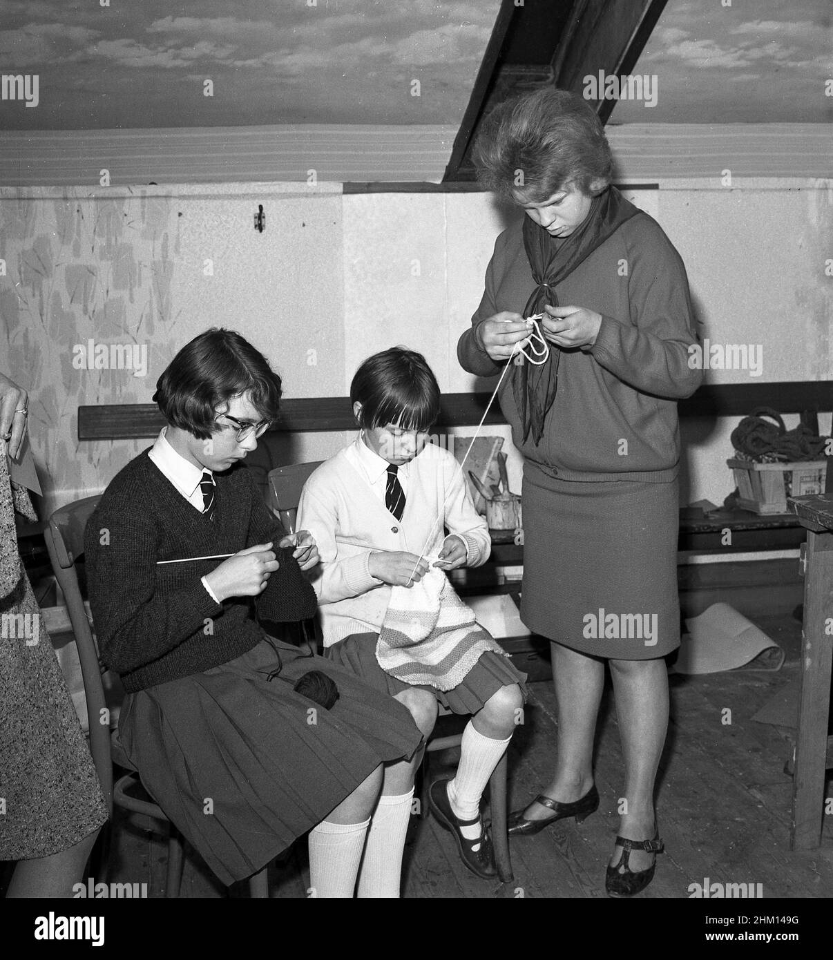 1960s, historisch, in einem Zimmer im Obergeschoss bei einem jungen Mädchen, zwei Schulmädchen, die auf Stühlen sitzen und stricken, zusammen mit einer jungen Jugendarbeiterin, die dabei hilft, die Wolle für das jüngere Mädchen zu halten, Fife, Schottland, Großbritannien. Stockfoto