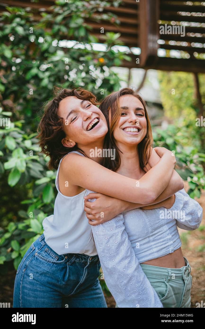 Zwei junge Teenager-Mädchen umarmten sich und lachten, umgeben von Pflanzen. Sie haben Spaß und scheinen sehr glücklich zu sein. Stockfoto