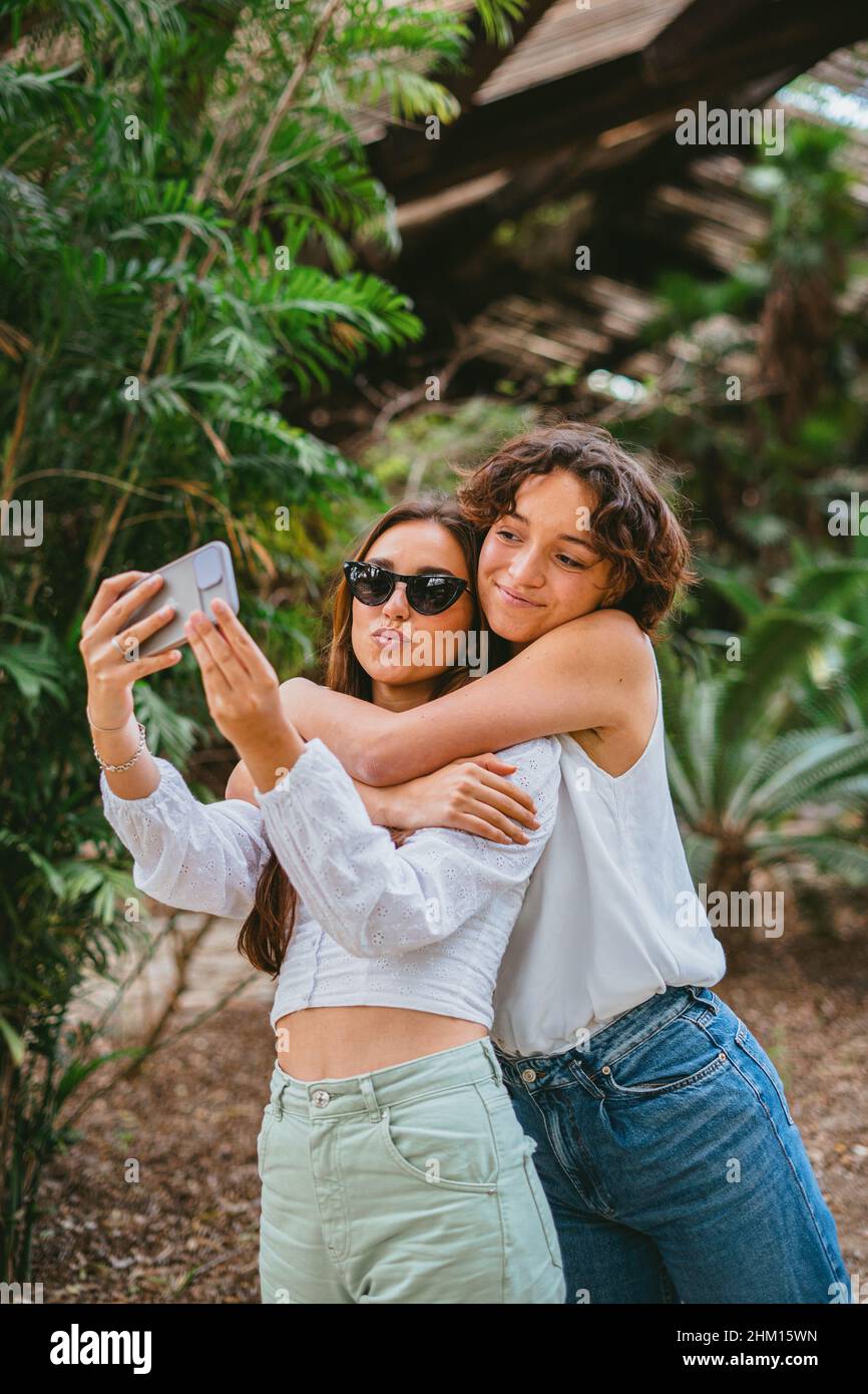 Zwei junge Teenager-Mädchen, die ein Selfie im Park machen, während sie sich umarmen. Sie haben Spaß und scheinen glücklich zu sein. Stockfoto