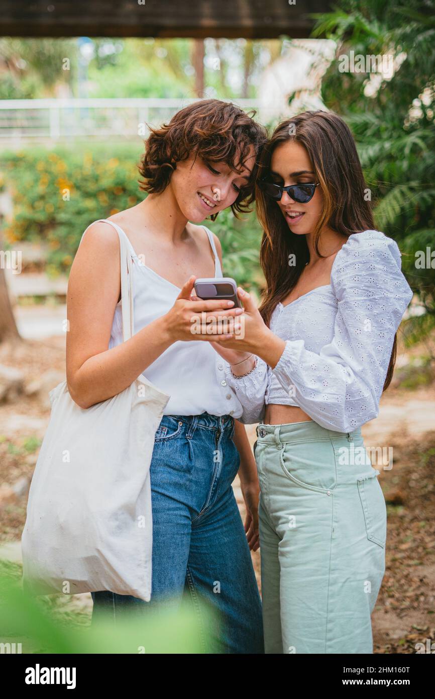 Zwei lächelnde Teenager-Mädchen, die auf ein Mobiltelefon blicken. Sie nutzen soziale Medien. Stockfoto