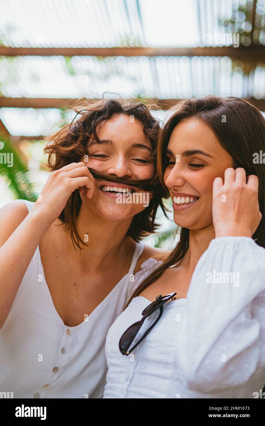 Zwei lustige Teenager-Mädchen, die Spaß im Park haben. Einer von ihnen spielt und macht Schnurrbart aus den Haaren eines anderen Mädchens. Stockfoto