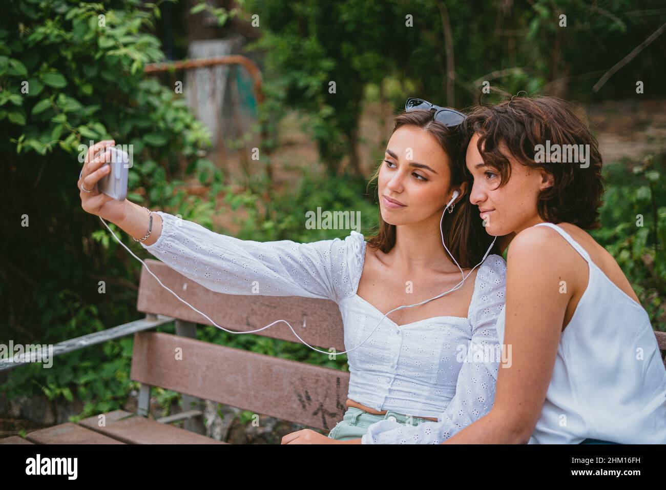 Zwei Mädchen im Teenageralter machen ein Selfie, während sie auf einer Bank in einem Park sitzen. Stockfoto