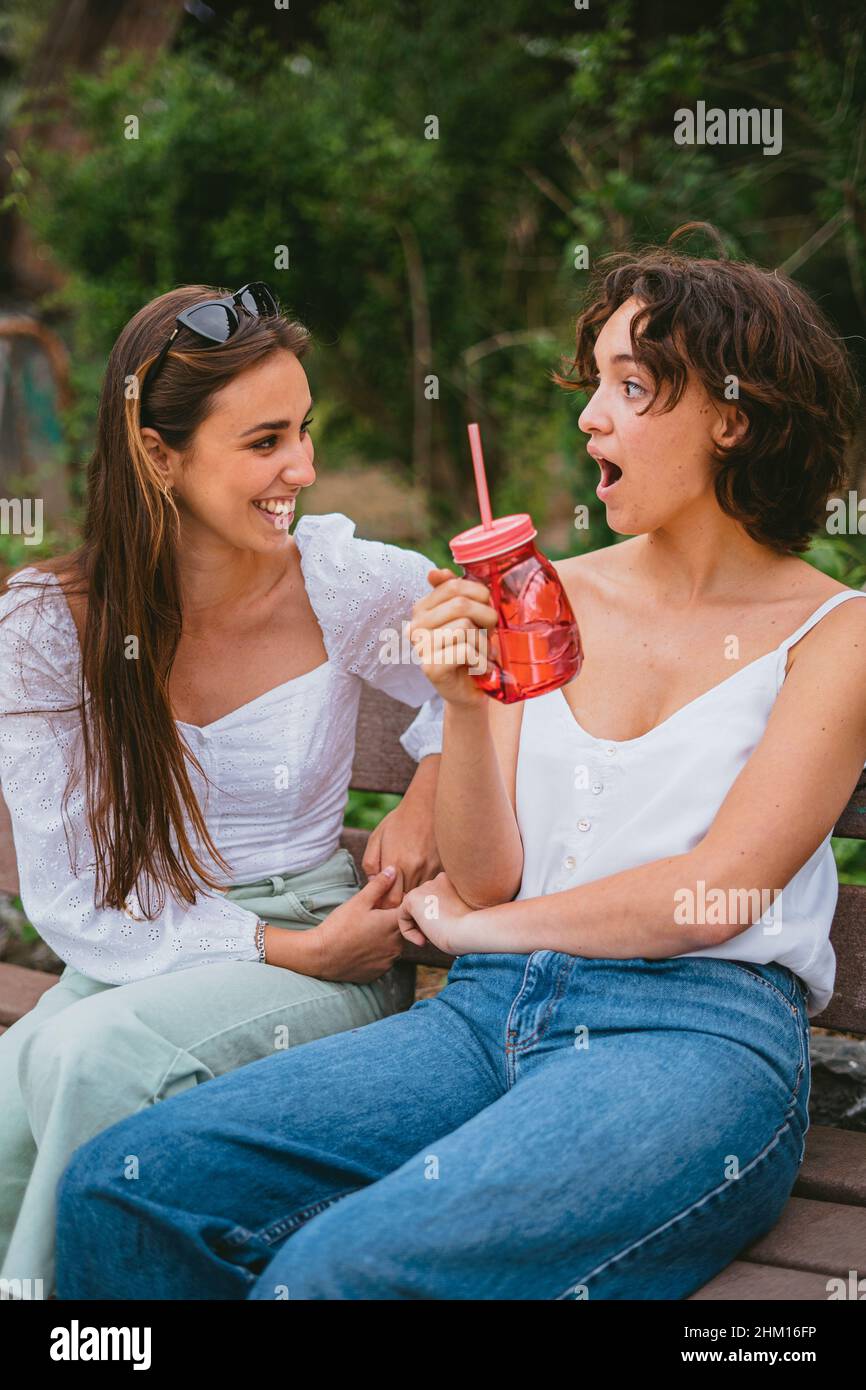 Zwei lächelnde Teenager-Freunde reden und lachen. Einer von ihnen hat ein rotes Glas und ist überrascht. Stockfoto