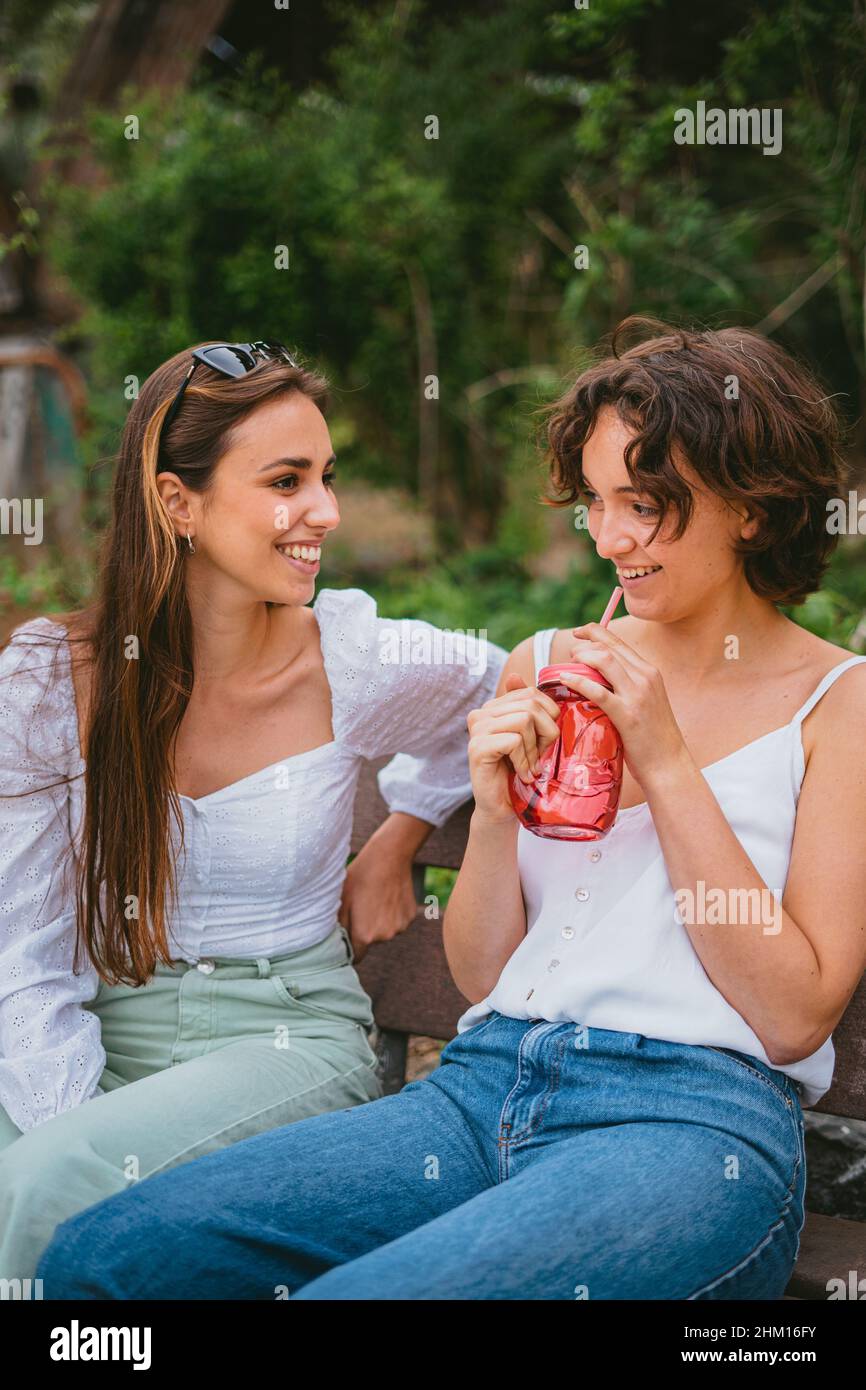 Zwei Teenager-Freunde lachen. Einer von ihnen trinkt einen Smoothie aus einem roten Glas. Stockfoto