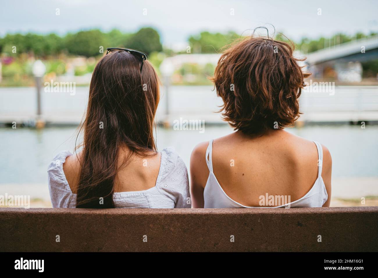 Zwei Teenager-Freunde sitzen auf einer Bank. Sie schauen auf den Fluss. Stockfoto