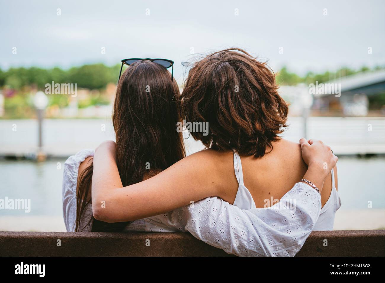 Rückansicht von zwei Teenagerfreunden, die auf einer Bank sitzen, während sie sich umarmen. Stockfoto