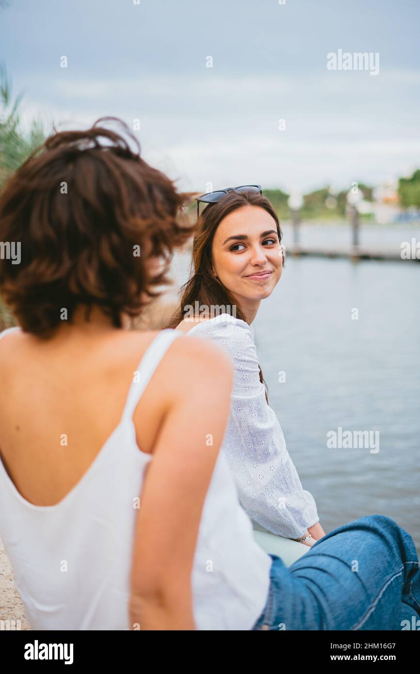 Zwei junge Frauen, die einander anguschauend sind. Sie sitzen am Fluss. Stockfoto
