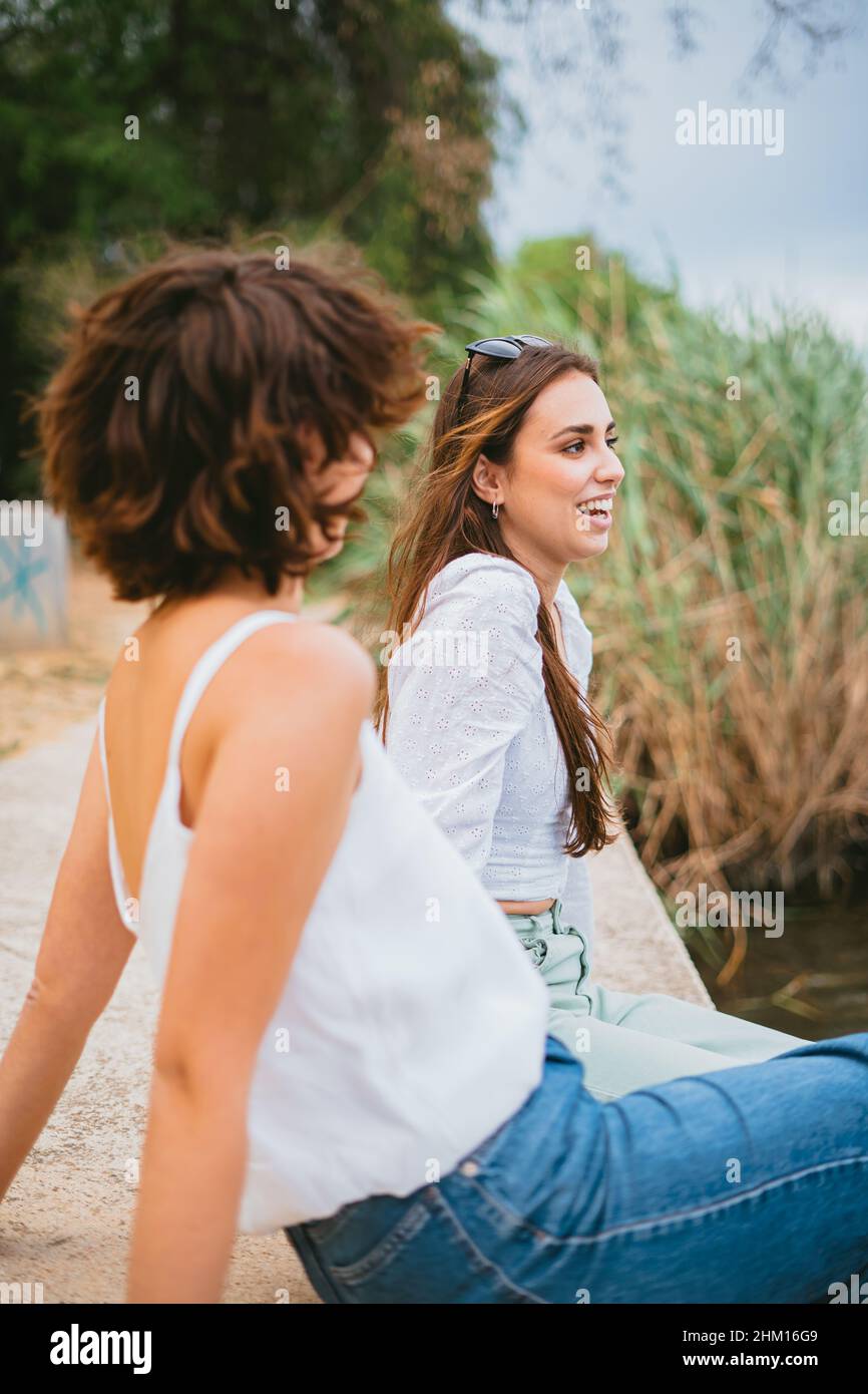Zwei Mädchen im Teenageralter reden und haben Spaß. Sie starren auf den Fluss. Es gibt einige Pflanzen und Sträucher im Hintergrund. Stockfoto