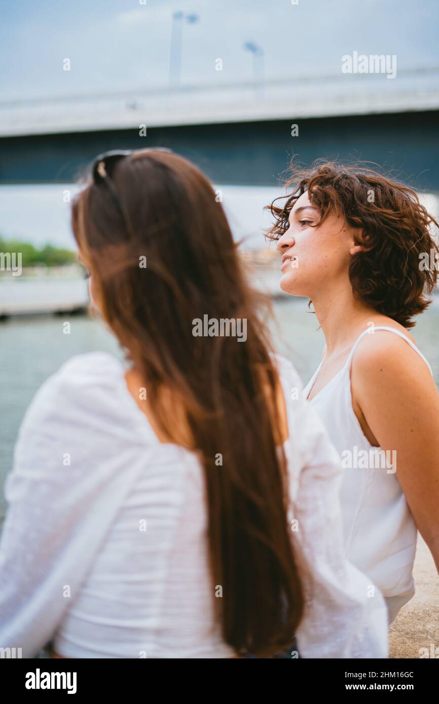 Zwei junge Frauen blicken auf den Fluss. Im Hintergrund befindet sich eine blaue Brücke. Stockfoto