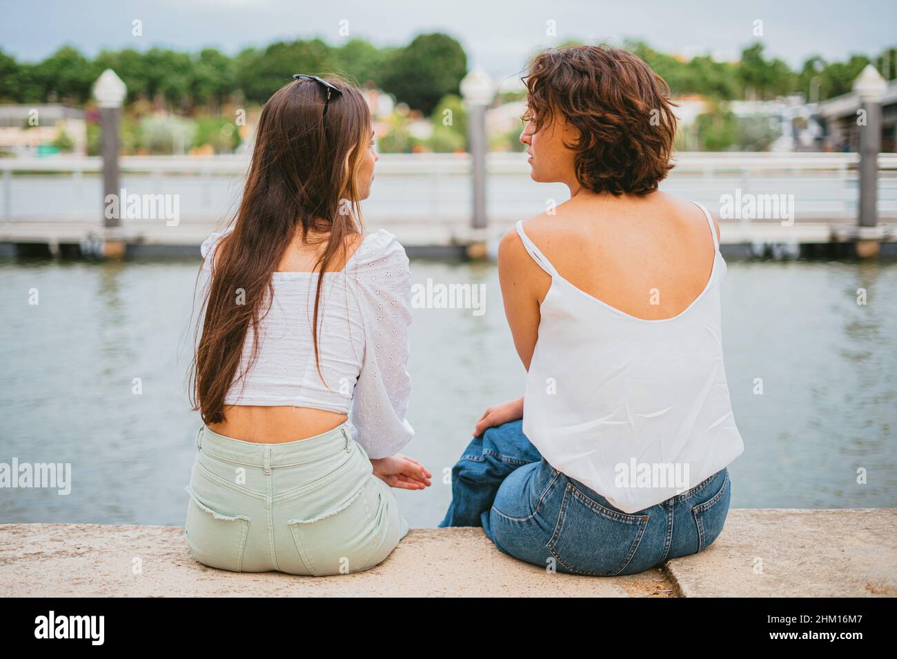 Rückansicht von zwei Teenagern, die an einem bewölkten Tag reden und den Fluss betrachten. Stockfoto