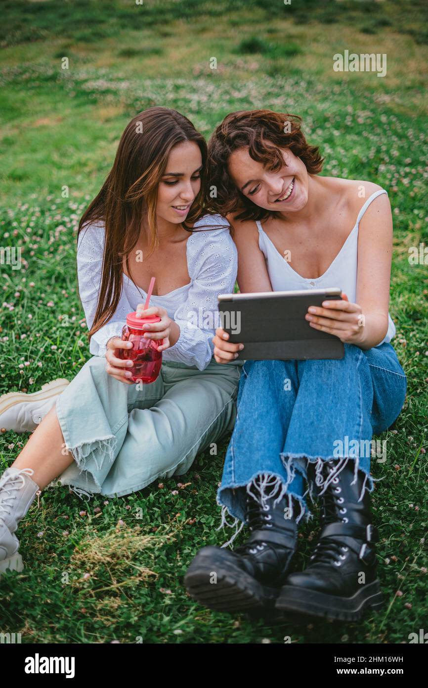 Zwei Freunde, die Spaß haben, ein Tablet zu betrachten, während sie sich auf dem Rasen des College-Campus ausruhen. Stockfoto