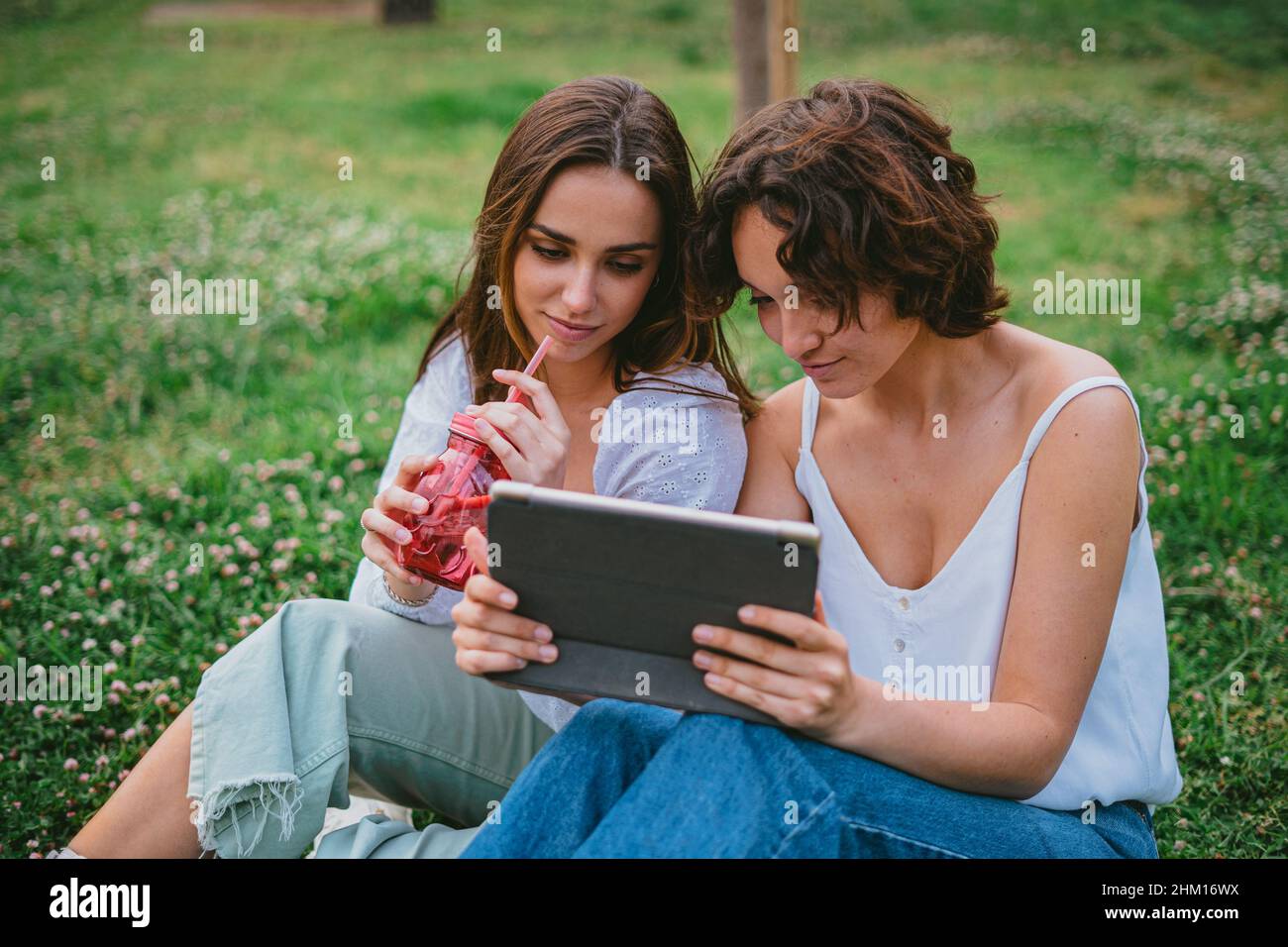 Zwei Jugendliche Studenten schauen sich im Park ein Video an, während sie sich vom Unterricht ausruhen Stockfoto