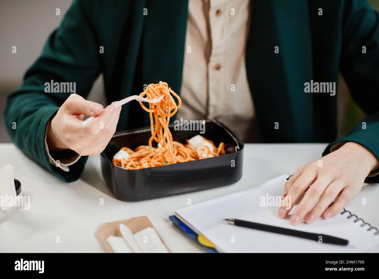 Hände einer jungen, zeitgenössischen Geschäftsfrau, die mitten im Arbeitstag einen leckeren chinesischen Wok in der Lunchbox hat, während sie am Schreibtisch sitzt Stockfoto
