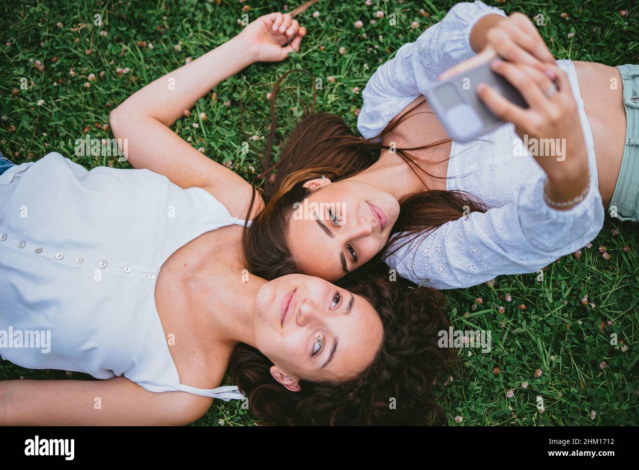 Zwei Freunde machen ein Selfie-Foto, während sie sich in einem Park auf dem Gras niederlegen. Stockfoto