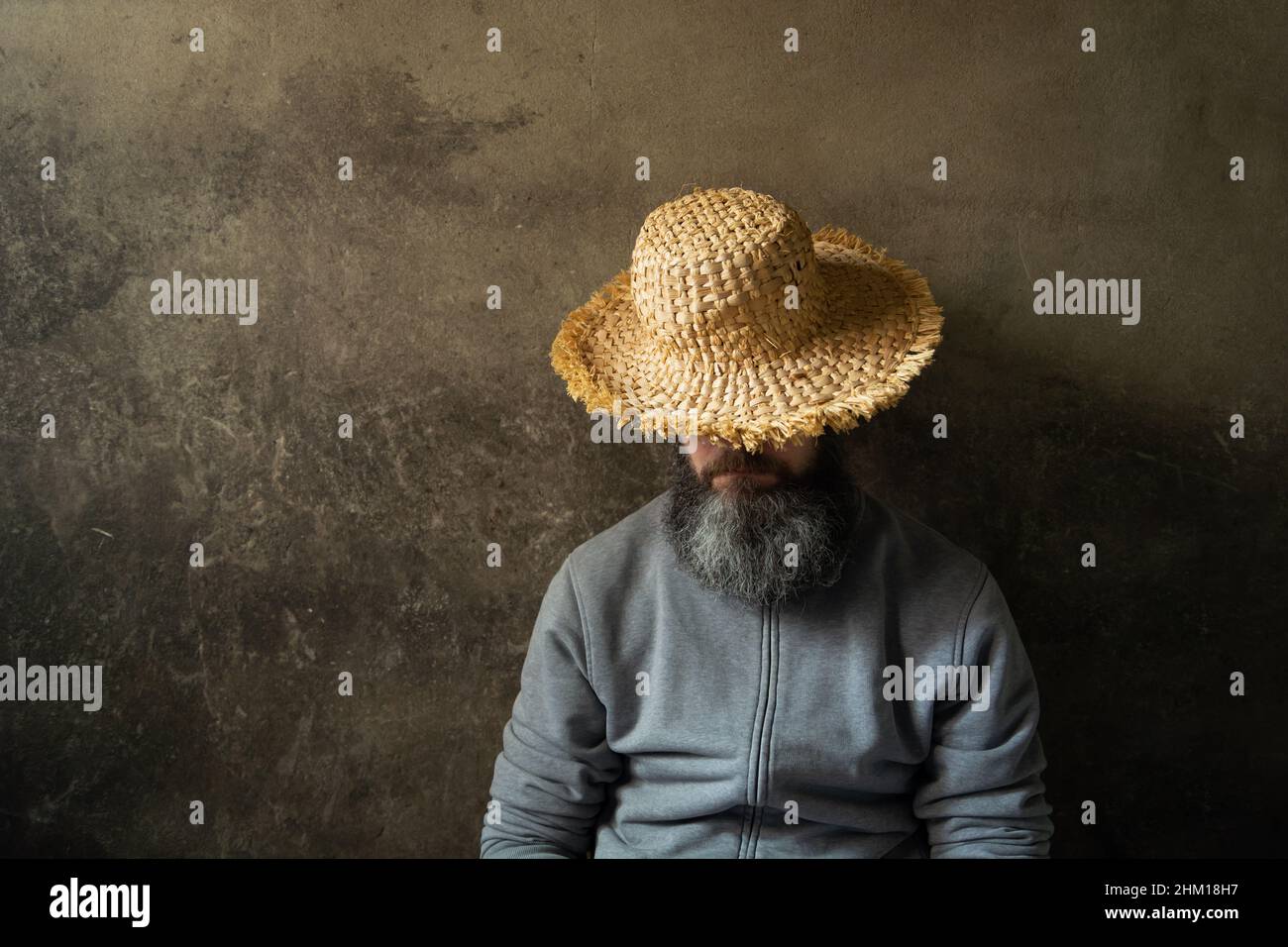 Ein schlampender Mann mit einem Bart in einem Hut vor dem Hintergrund einer dunklen Wand Stockfoto
