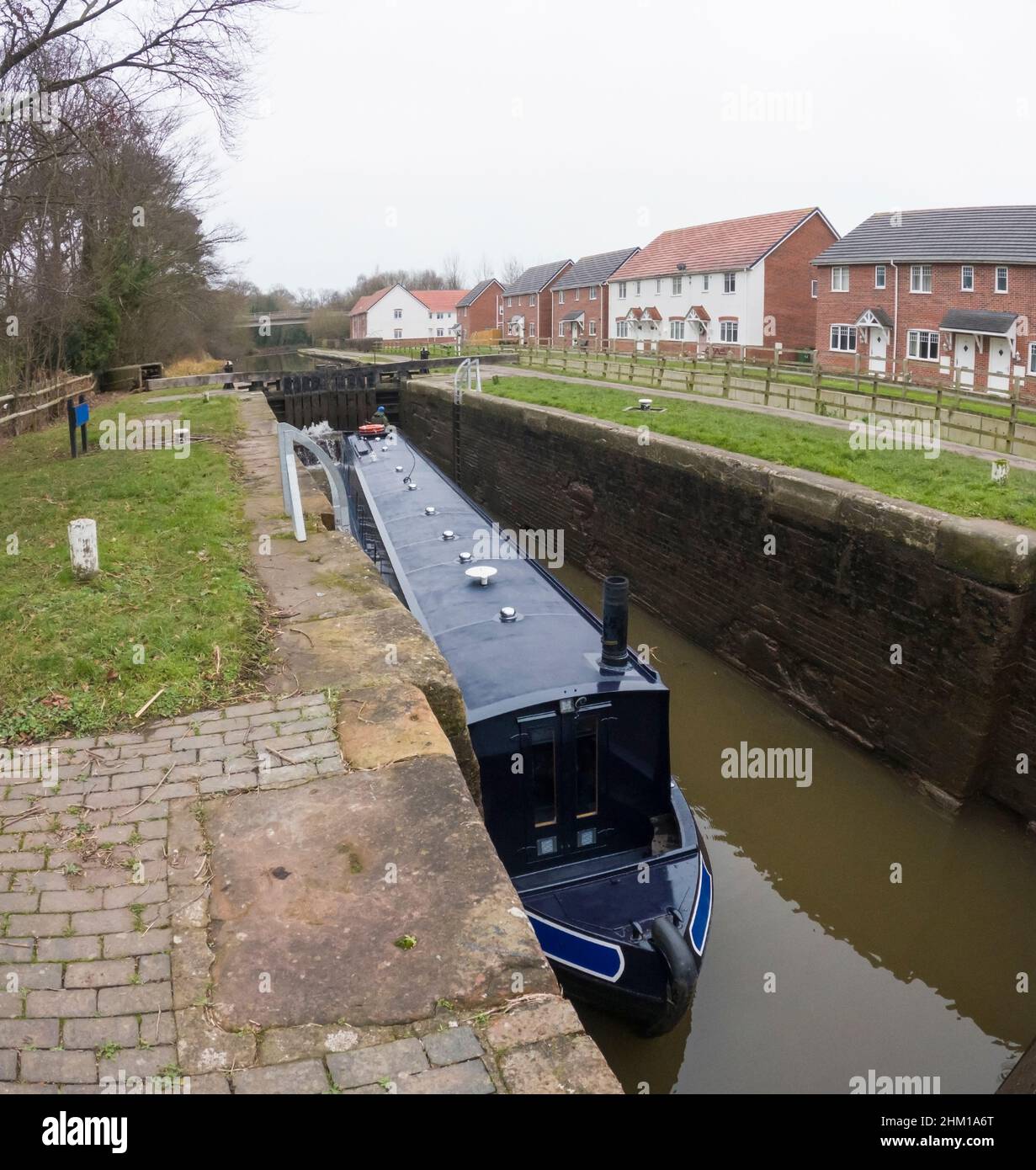 Narrowboat, das durch eine tiefe Schleuse in der ländlichen Landschaft Englands auf dem britischen Wasserstraßenkanal fährt Stockfoto