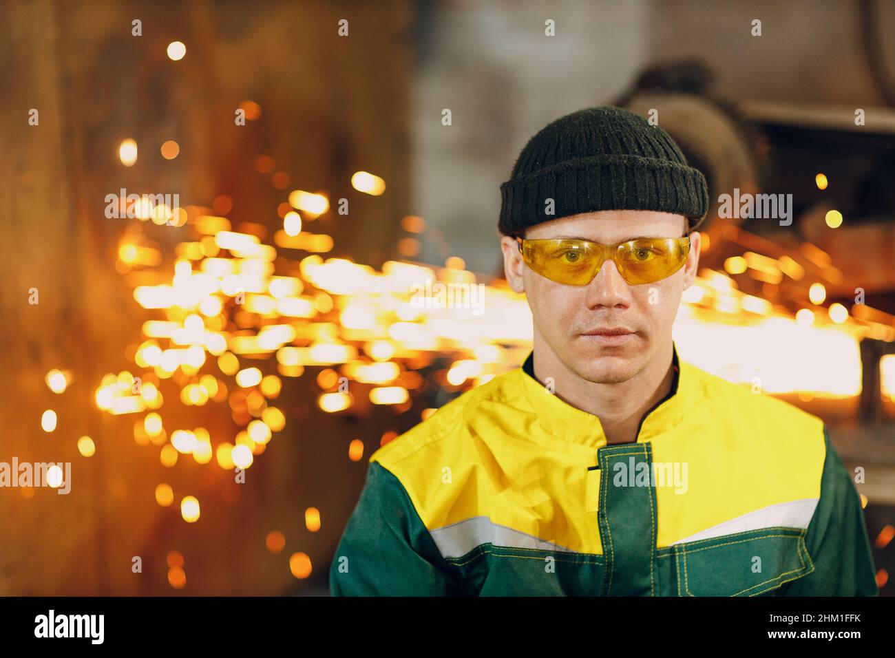 Porträt eines Arbeiter-Ingenieurs in einer einheitlichen Schutzbrille mit Werkshintergrund und Funkenflug Stockfoto