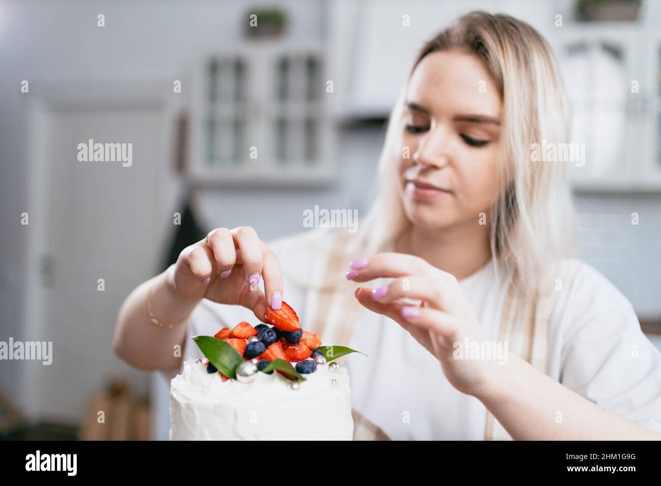 Konditor Konditor junge kaukasische Frau dekorieren Kuchen auf Küchentisch. Kuchen Cupcakes und süßes Dessert Stockfoto