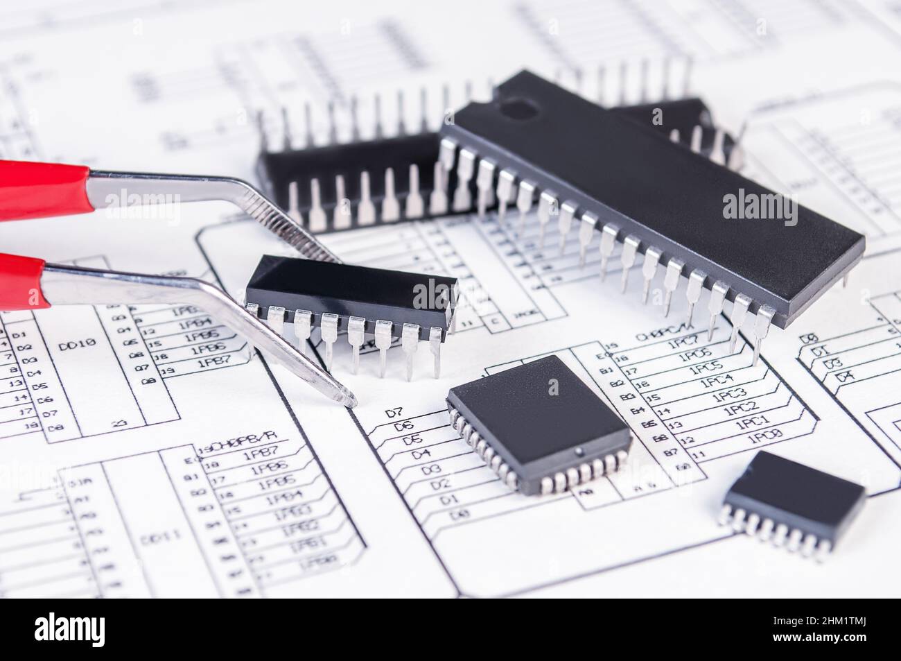 Elektronikkomponenten und Pinzetten auf dem Hintergrund des Schaltplans. Konzept für die Entwicklung und Konstruktion von elektronischen Geräten. Stockfoto