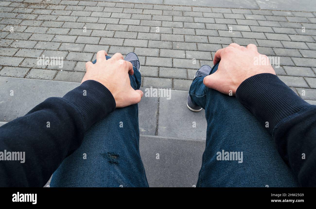 Der Mann sitzt auf einem Randstein und wartet nervös auf jemanden, aus der Perspektive geschossen Stockfoto