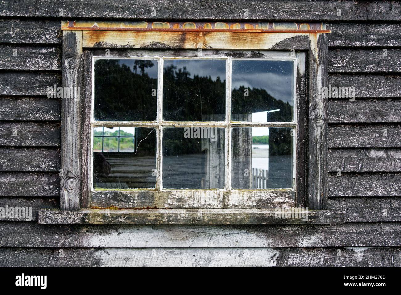 Ein Glasfenster in einem Holzschuppen, das eine Renovierung und Renovierung überfällig ist. Stockfoto