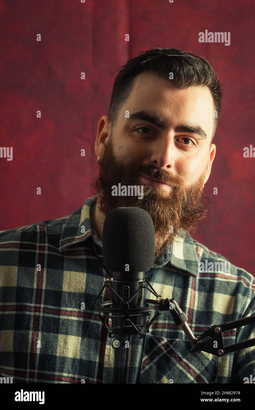 Junger Hipster-Mann in der Nähe eines Streaming-Mikrofons, der mit einem roten Hintergrund lächelt und Platz zum Kopieren hat Stockfoto