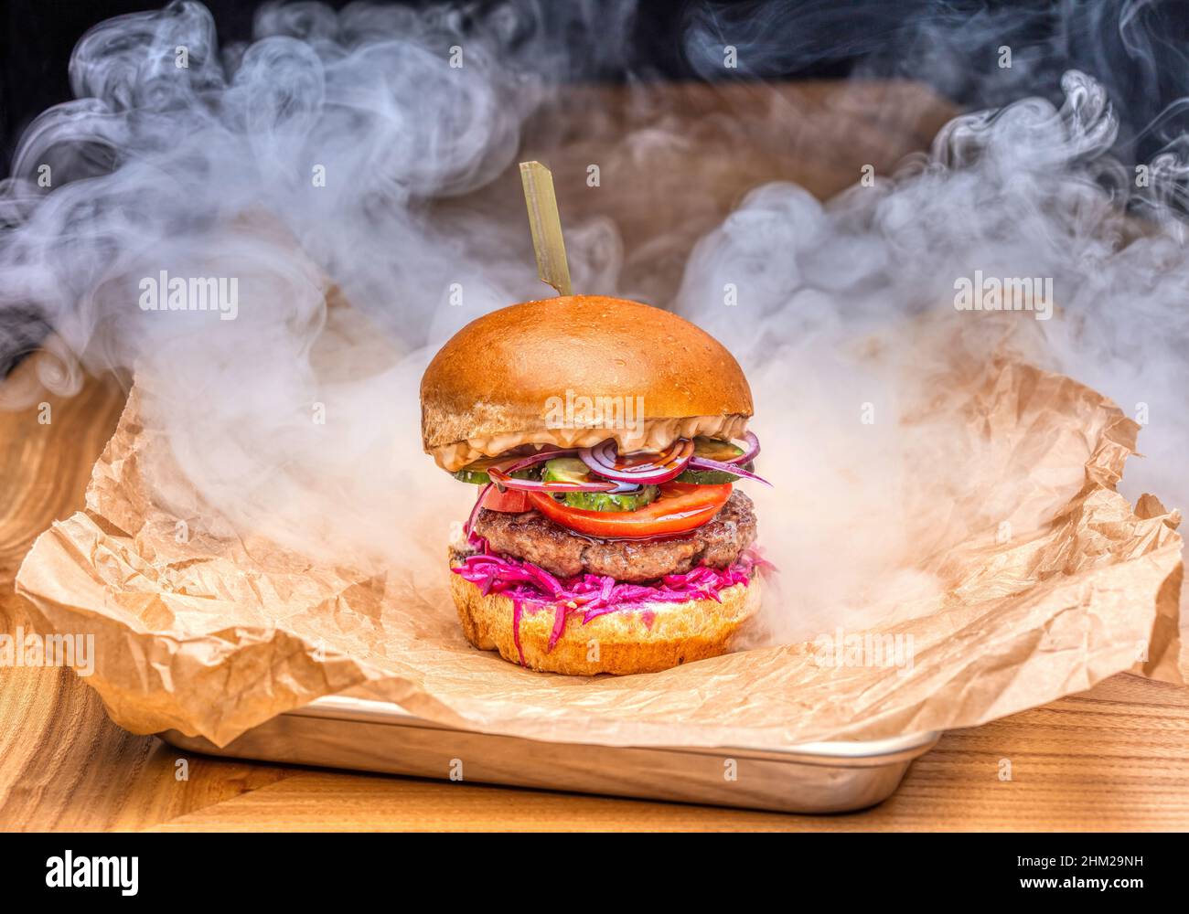 Köstlicher saftiger Burger mit Rauch auf einem Holztisch Stockfoto