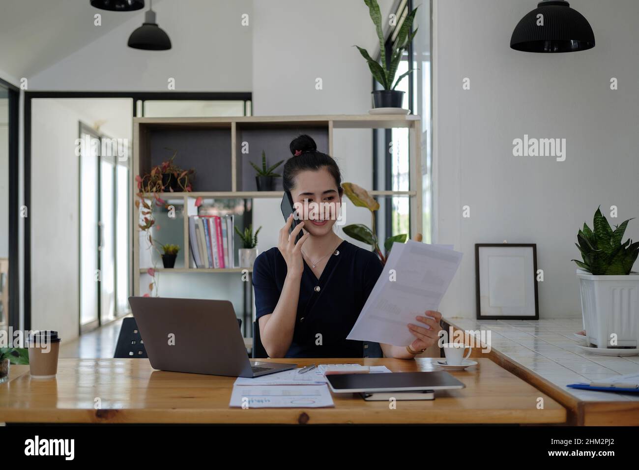 Junge asiatische Geschäftsfrau schöne charmante lächeln und sprechen auf dem Handy arbeiten mit Papierkram Finanzdiagramm Diagramm im Büro Stockfoto
