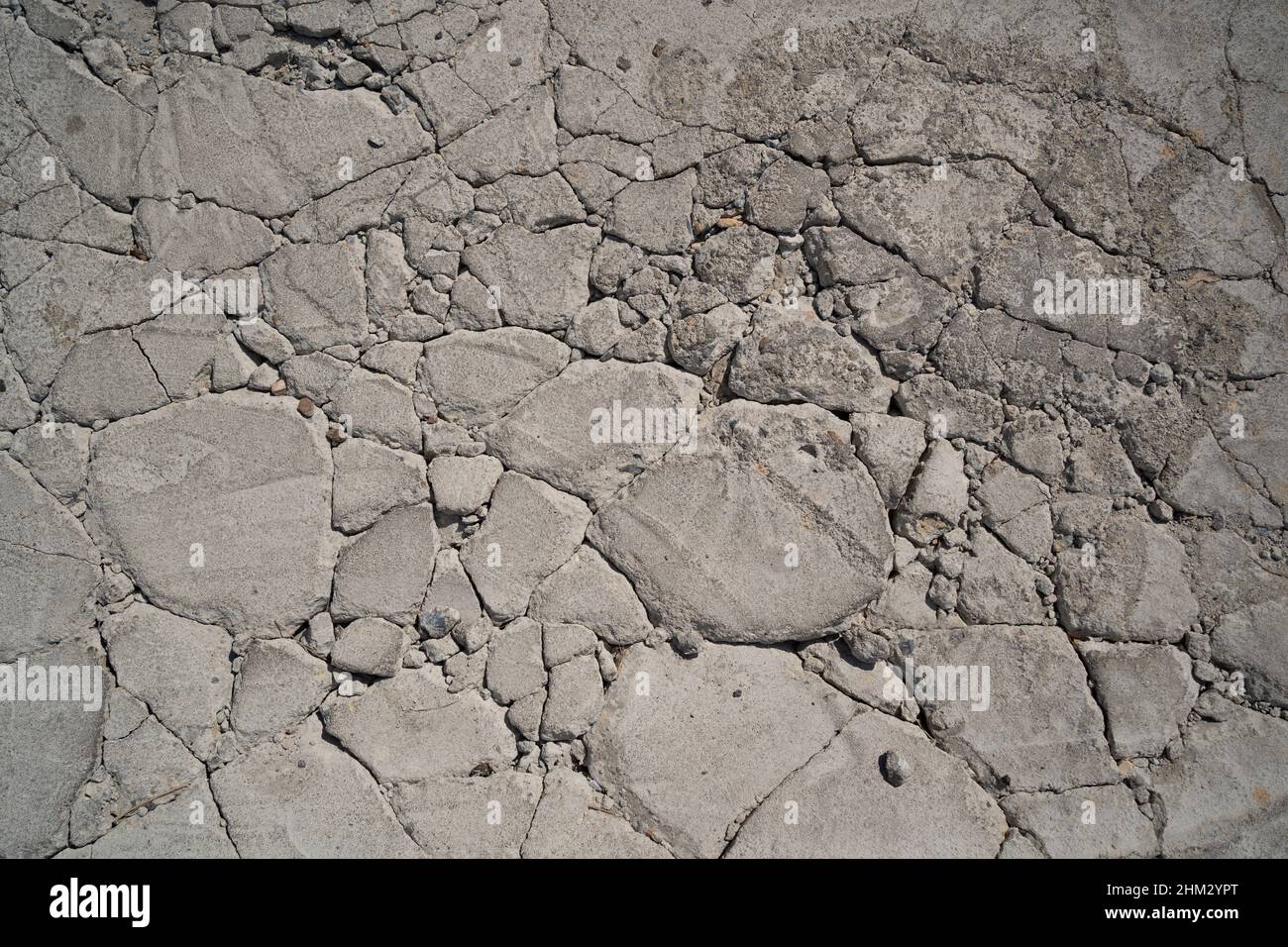 Grauer Betonboden, der in einen zufällig großen Gesteinshintergrund gesprungen ist Stockfoto