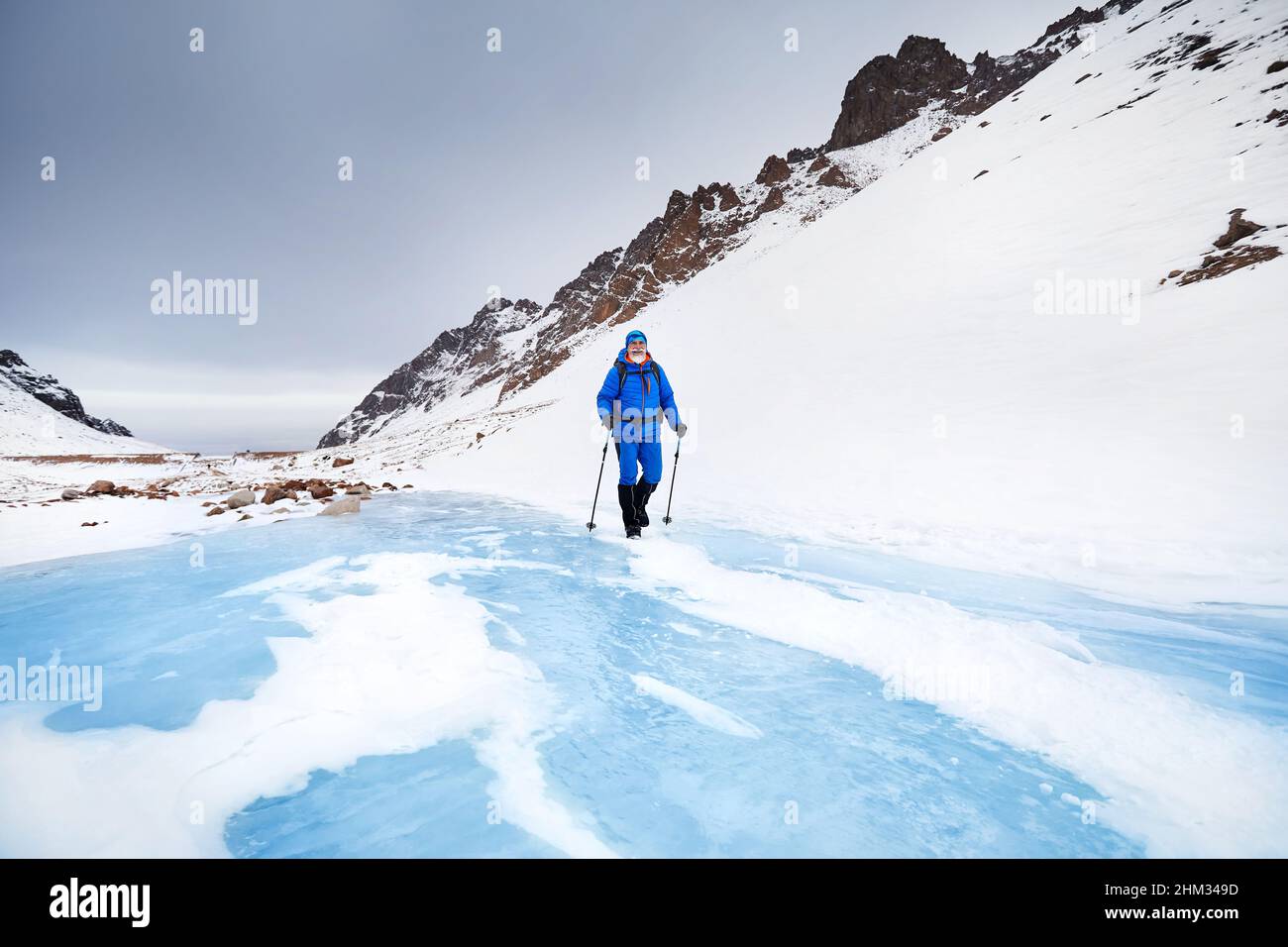 Tourist mit weißem Bart und Rucksack zu Fuß auf blauem Eis Gletscher in der wunderschönen Landschaft des Gebirgstals mit Schnee bedeckt in Almaty, Kasachstan Stockfoto